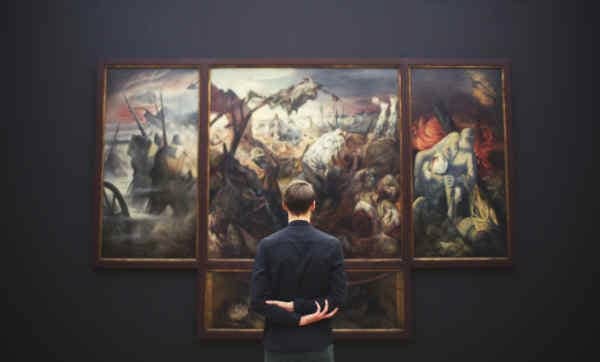 Man looking at large paintings in a museum.